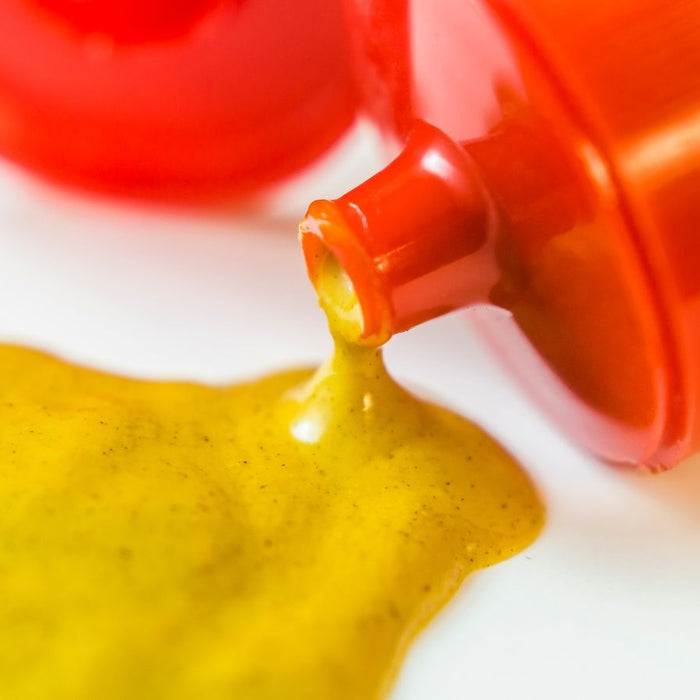 Yellow mustard pouring from squeeze bottle onto white surface.