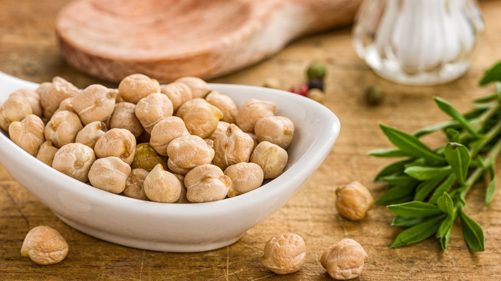 Dry chickpeas in white bowl on wooden table with herbs