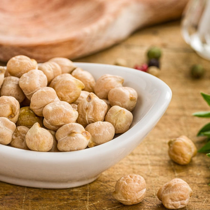 Dry chickpeas in white bowl on wooden table with herbs