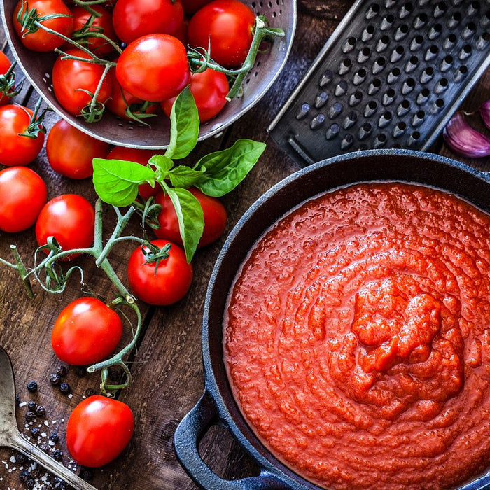Tomato sauce in a pan with fresh tomatoes and cooking ingredients.