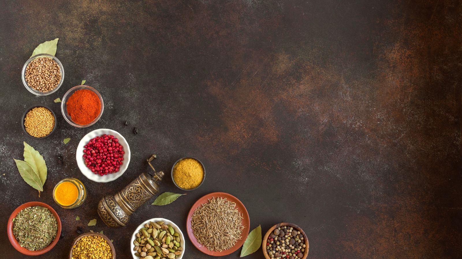 Collection of herbs and spices in bowls on rustic dark background