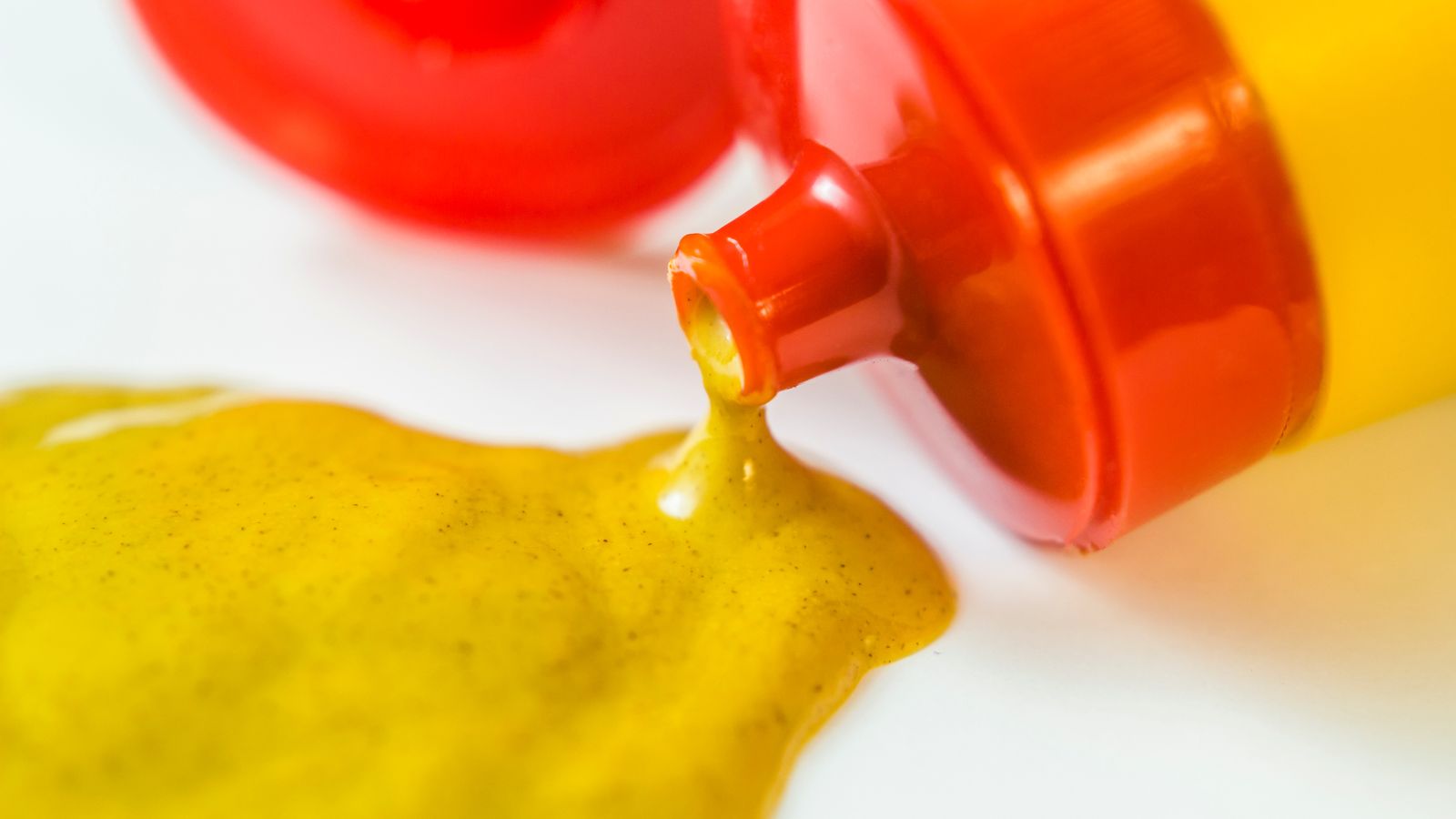 Yellow mustard pouring from squeeze bottle onto white surface.