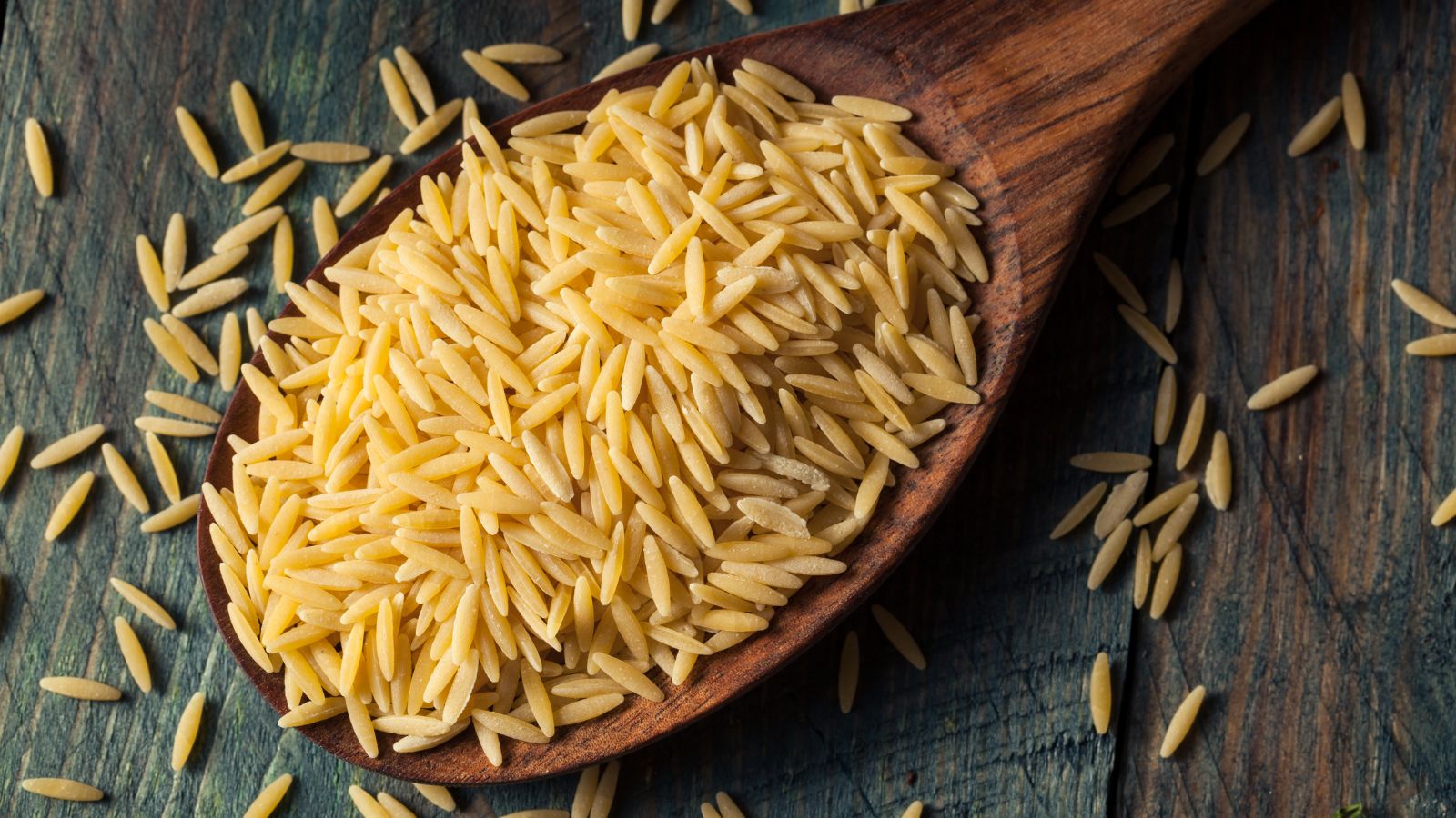 Uncooked orzo pasta grains in a wooden spoon on rustic wooden table
