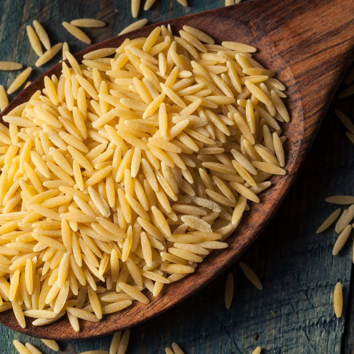Uncooked orzo pasta grains in a wooden spoon on rustic wooden table
