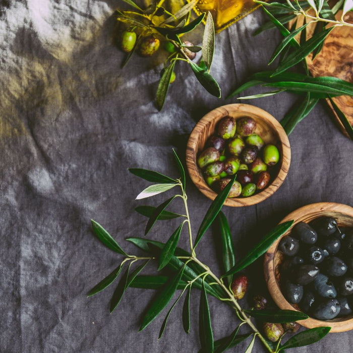 Rustic wooden bowls of green and black olives accompanied by olive sprigs.