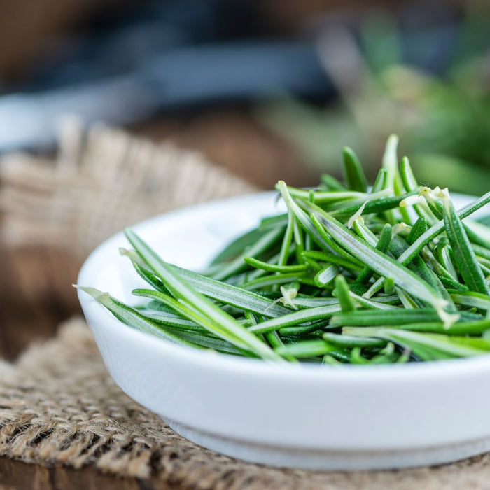 Fresh rosemary sprigs in a white bowl on rustic wooden table surface