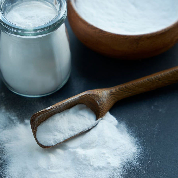 Baking soda in glass jars and wooden spoon on dark background.