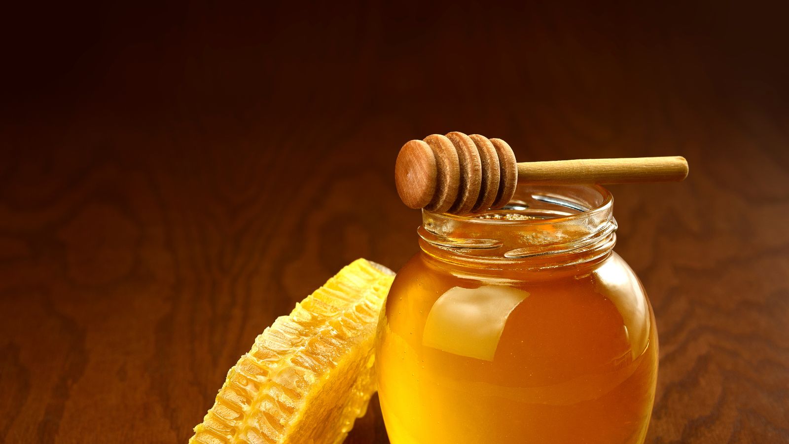 Jar of golden honey with honeycomb and a wooden dipper.