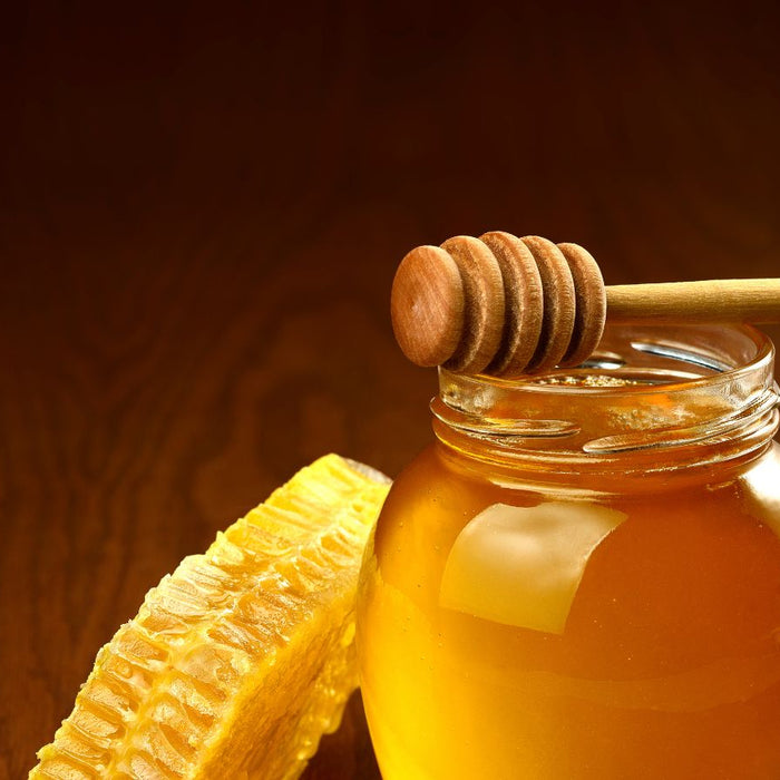 Jar of golden honey with honeycomb and a wooden dipper.