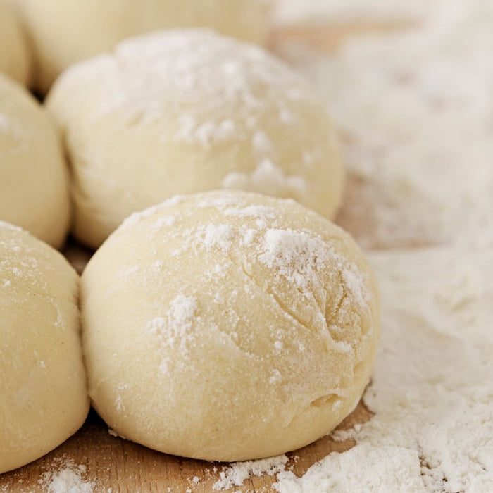 Dough balls covered in flour on wooden surface.