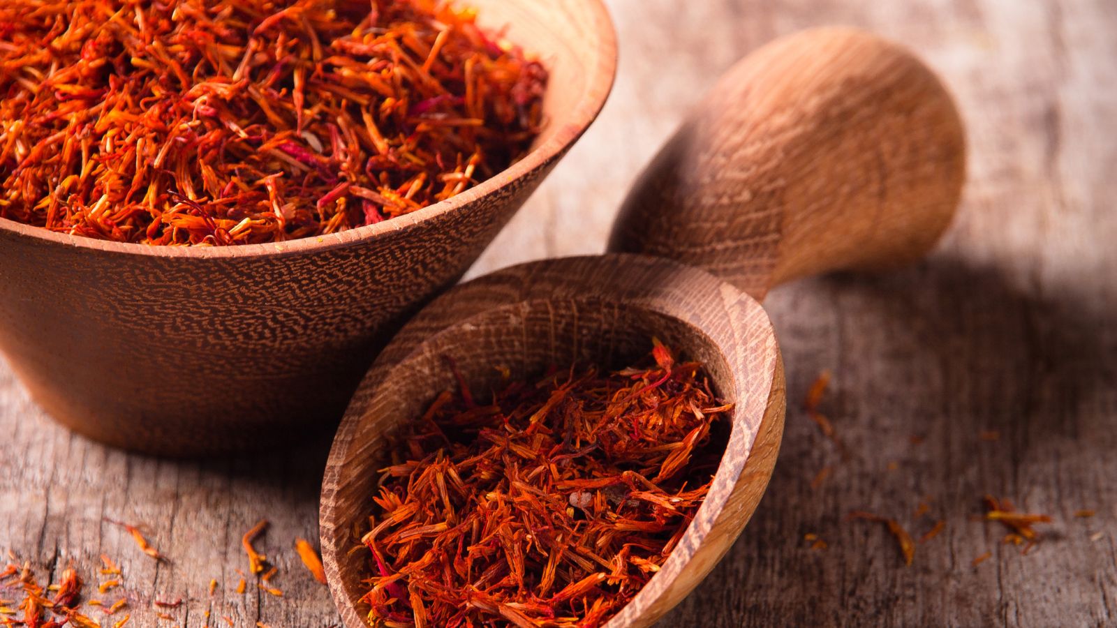 Dried saffron threads in a wooden bowl on a rustic wooden table.