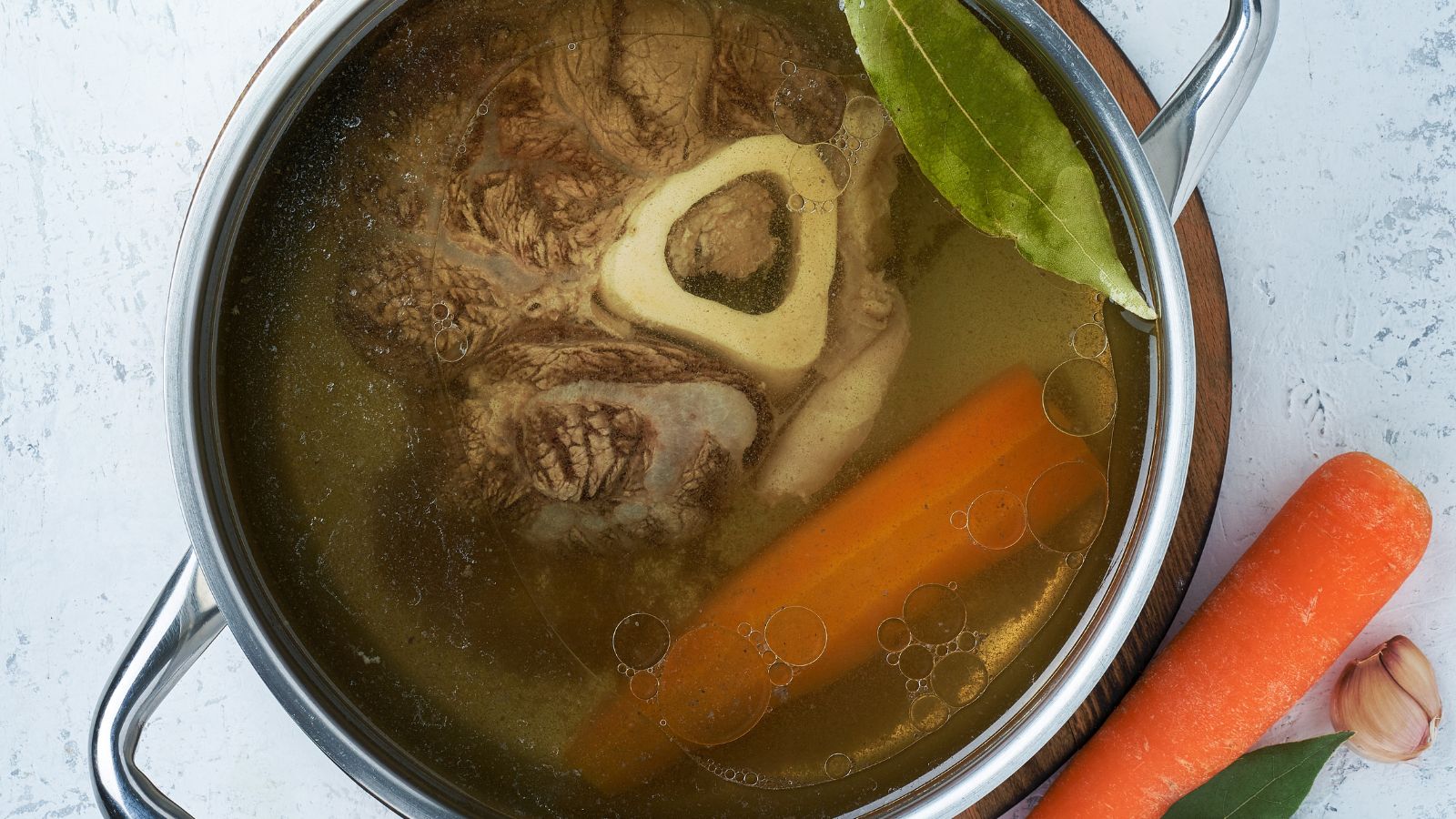 Pot of bone broth with beef marrow, carrots, garlic, and bay leaf.