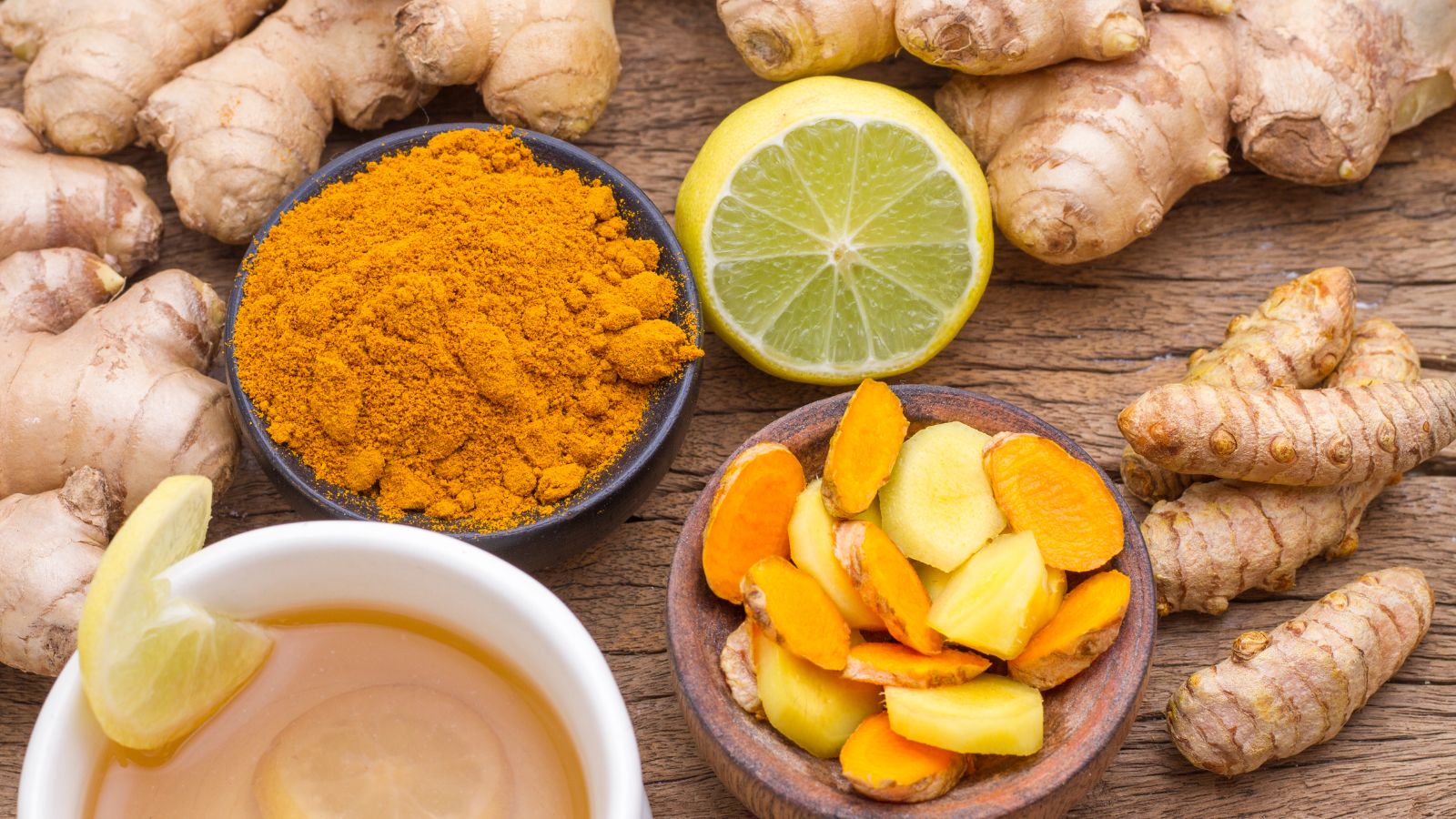 Turmeric, ginger, lemon slices, and tea arranged on rustic wood table