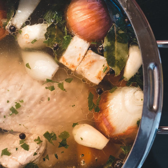 Chicken bone broth simmering with onion, herbs, and vegetables.