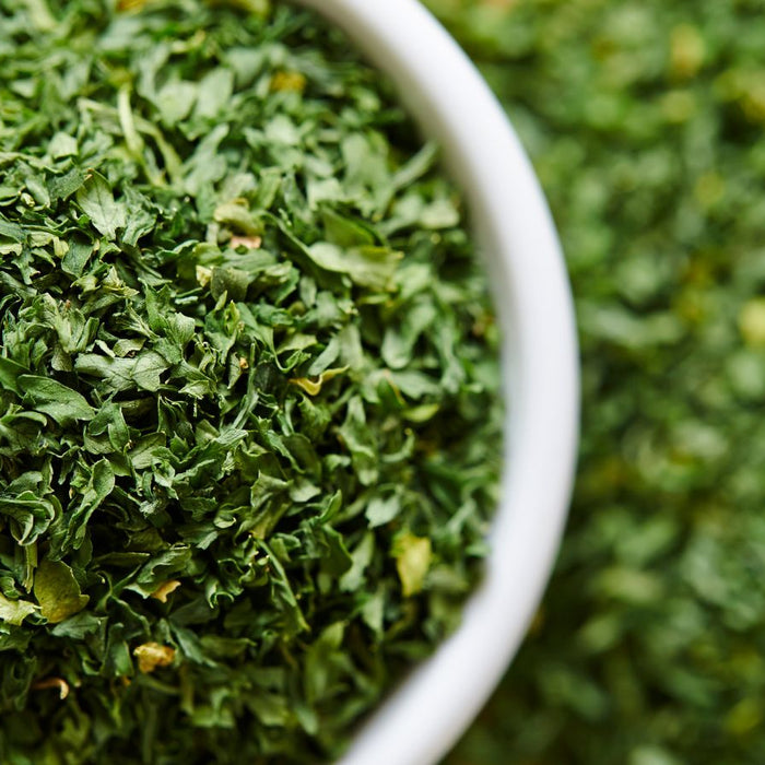 Close-up of dried parsley flakes in white bowl on green background.