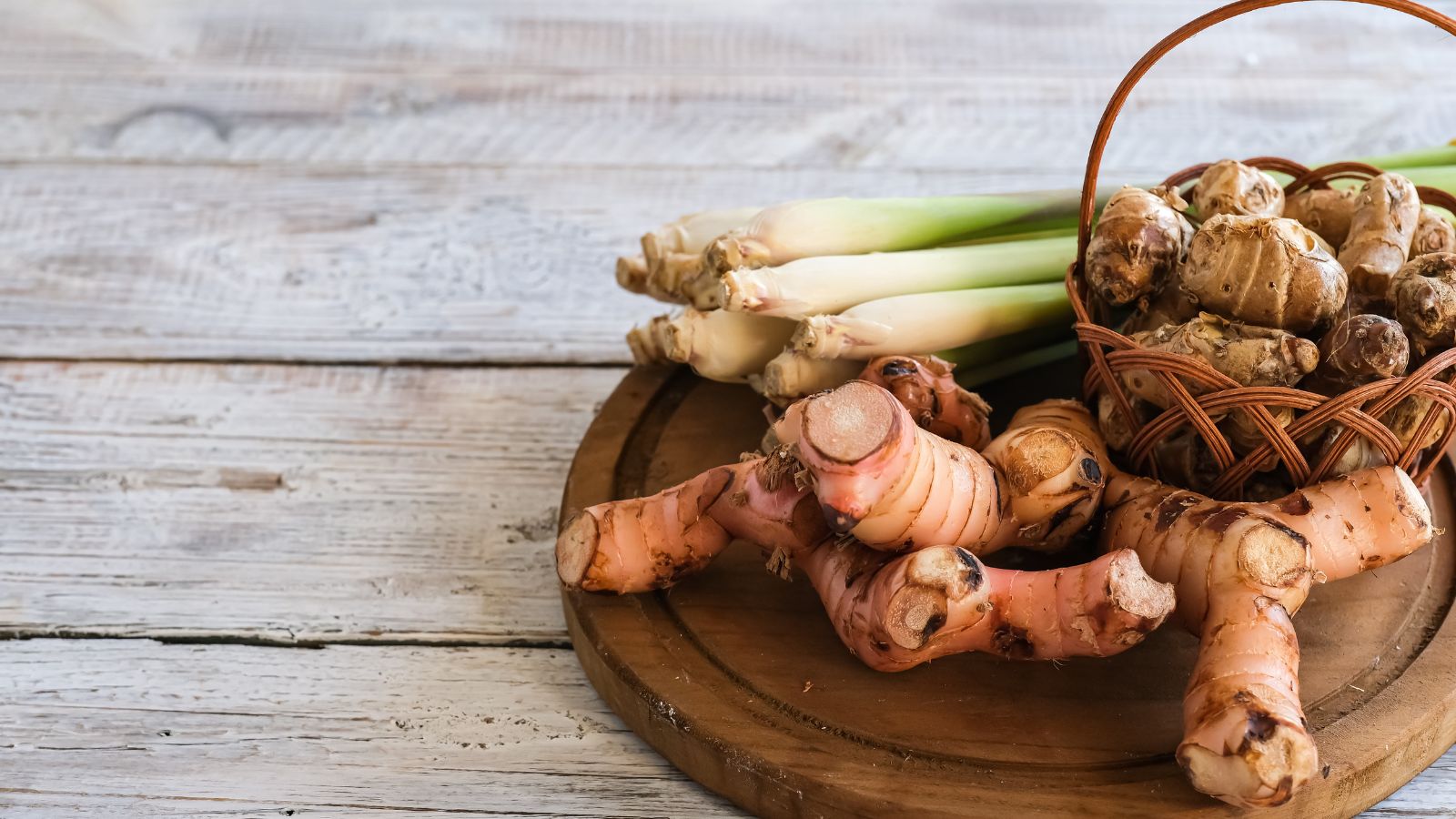 Fresh ginger roots and lemongrass stalks on wooden round board