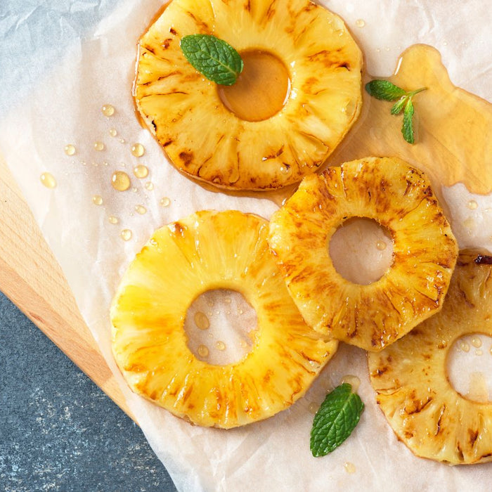 Grilled pineapple rings drizzled with syrup and mint leaves.