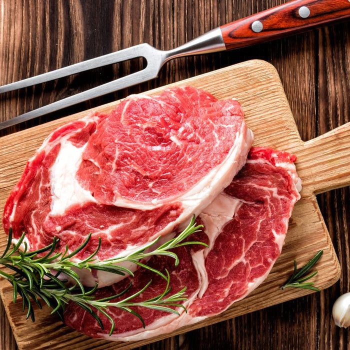 Raw ribeye steaks on wooden board with garlic and rosemary.