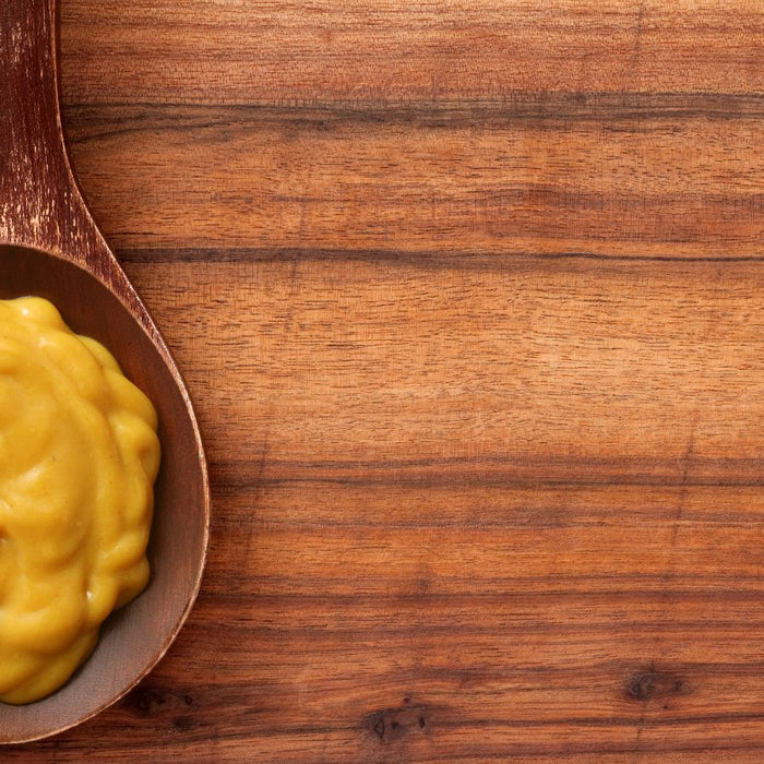 Brown mustard served on wooden spoon on wood background.