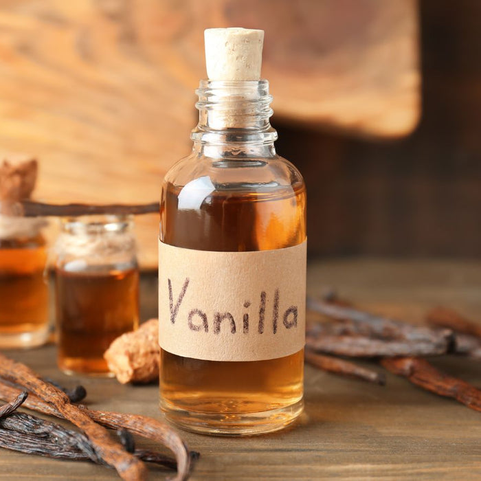 Vanilla extract bottle with vanilla beans on wooden background.