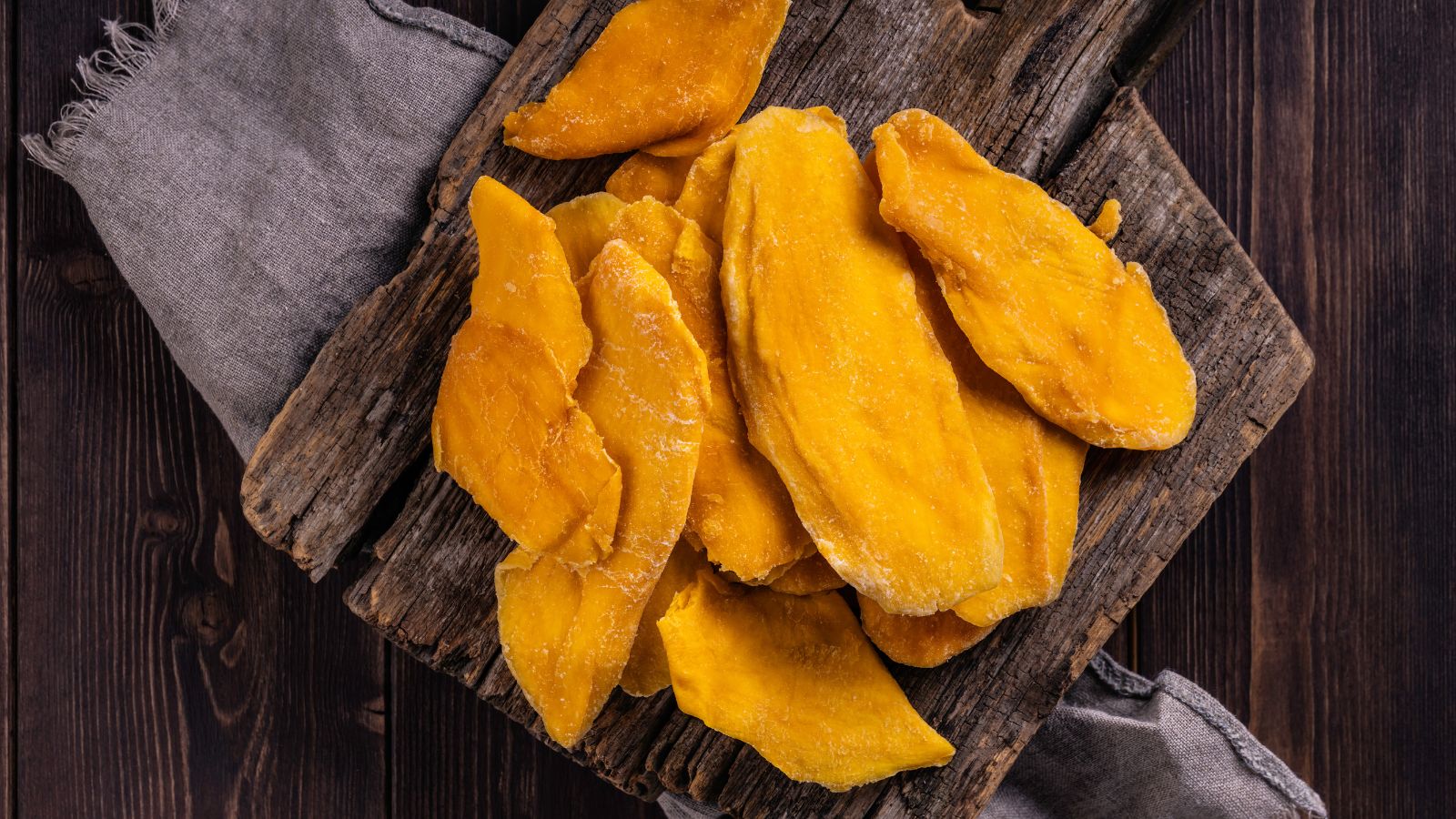 Close-up of dried mango slices on rustic wooden board.