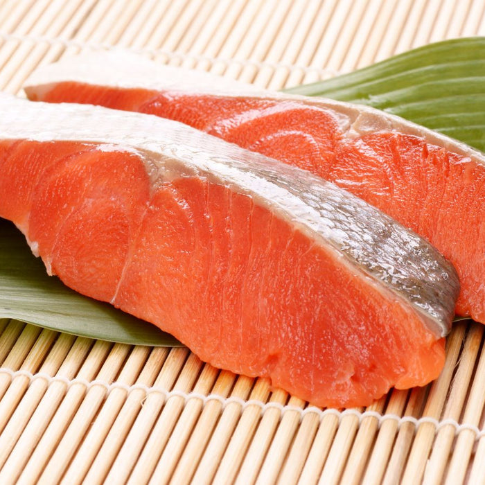 Fresh raw salmon fillets on bamboo mat and green leaf for sushi.