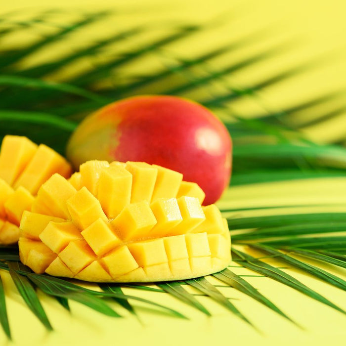 Two hedgehog-style mango halves and whole mango on palm leaf backdrop.