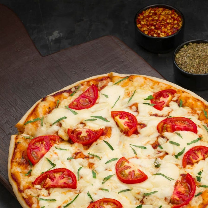 Tomato and cheese pizza on wooden board with herbs and spices bowls.