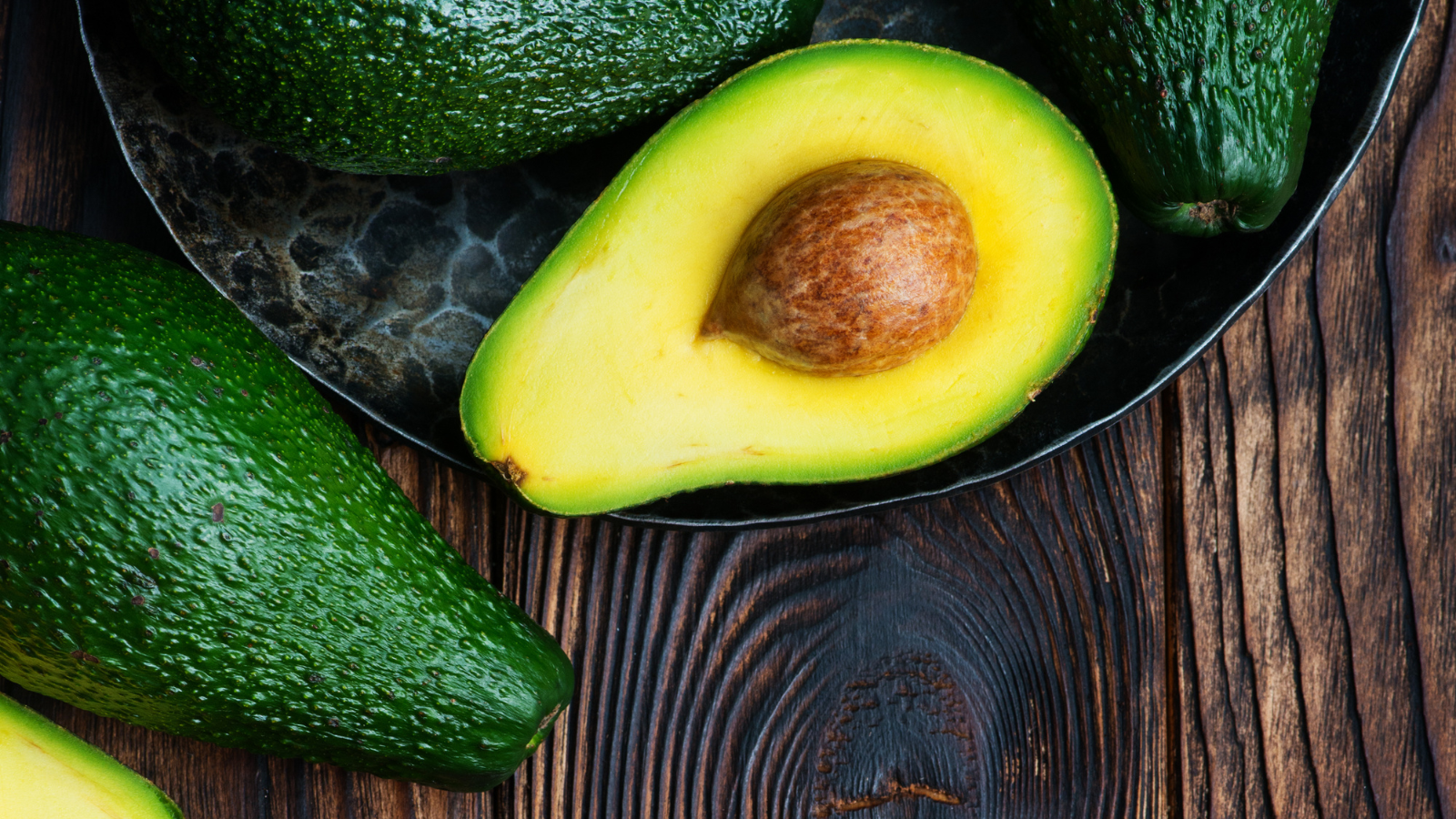 Ripe avocado cut in half with seed on rustic wooden background plate.