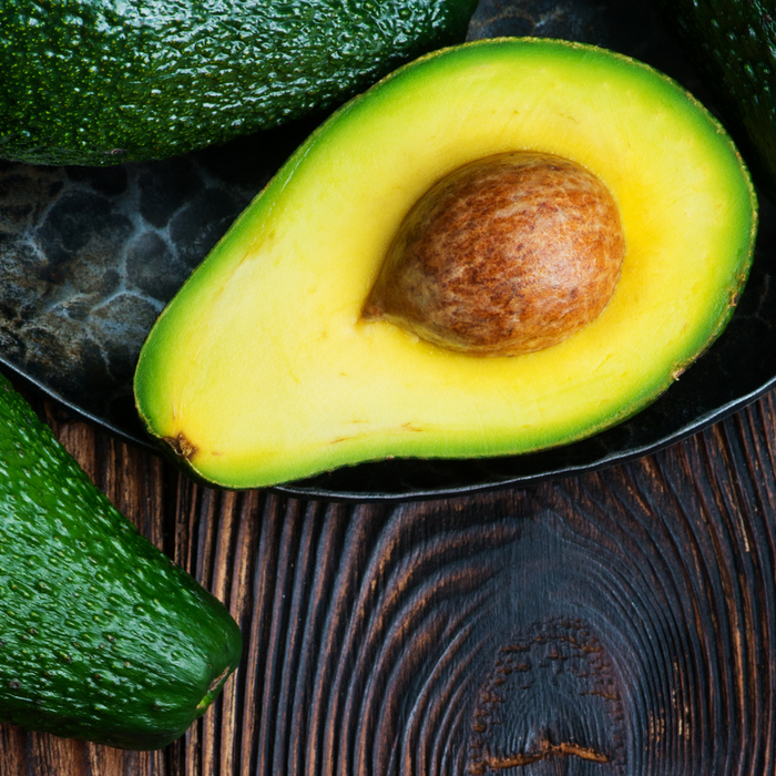 Ripe avocado cut in half with seed on rustic wooden background plate.