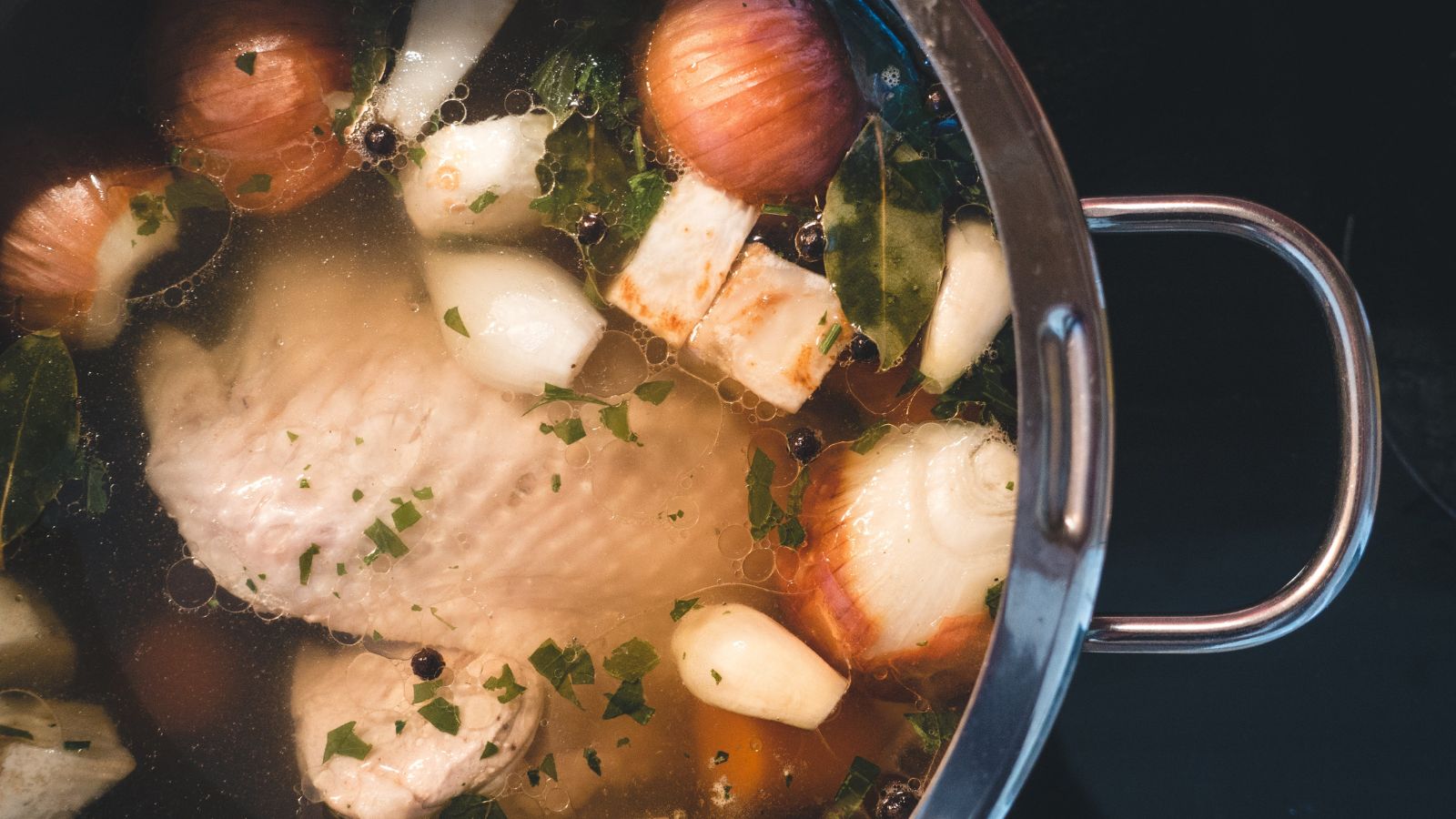 Chicken bone broth simmering with onion, herbs, and vegetables.