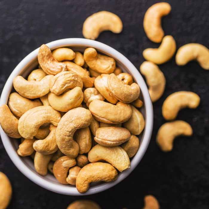 Bowl of roasted cashew nuts on dark surface with scattered pieces.