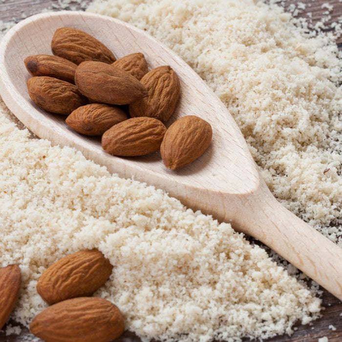 Wooden spoon with almonds rests on pile of almond flour on rustic wood.