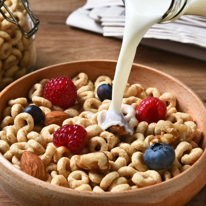 Milk pouring into a bowl of cereal with berries and mixed nuts.