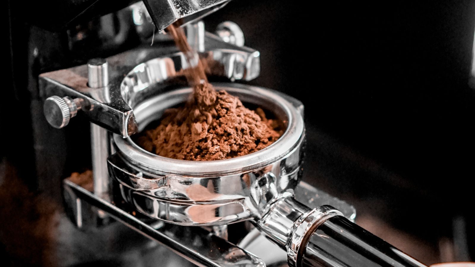 Espresso machine dispensing freshly ground coffee into portafilter.