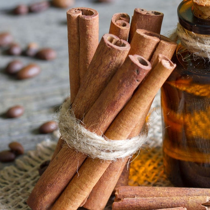 Cinnamon sticks with amber bottle on wooden surface.