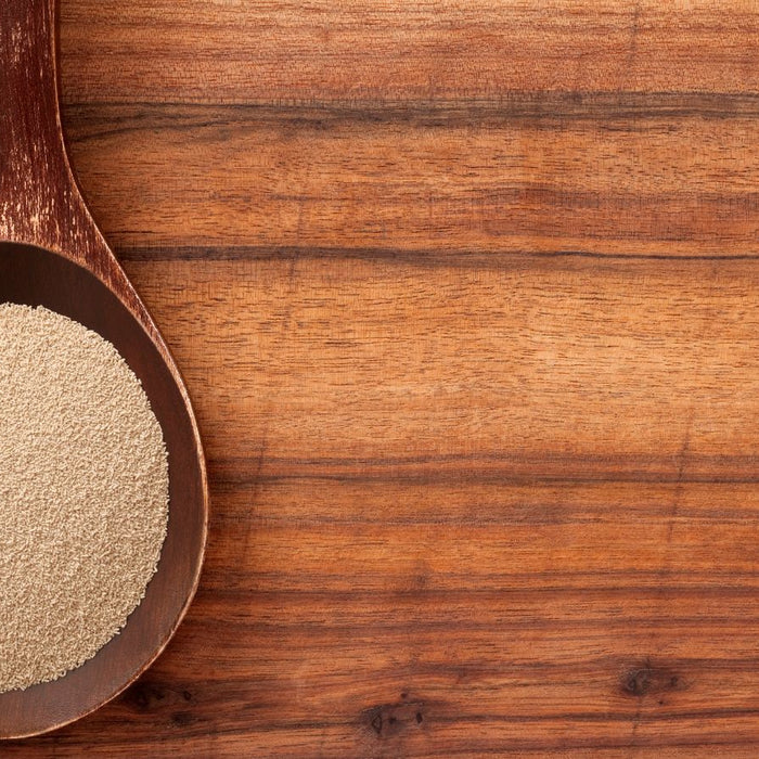Wooden spoon filled with dry active yeast on wooden table.