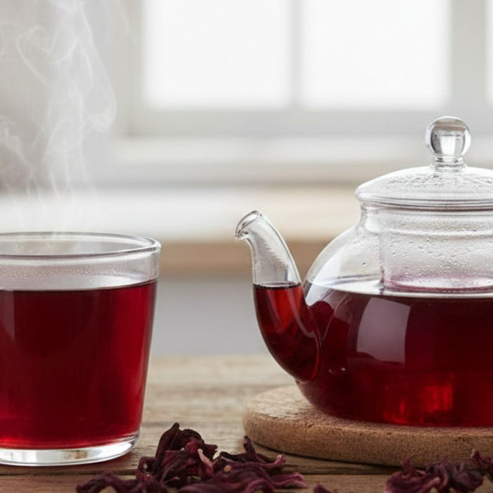 Steaming cup and glass teapot filled with hibiscus tea