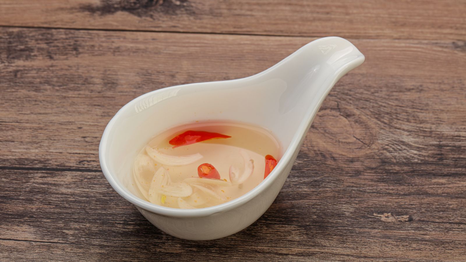 Vinegar fish sauce with garlic and chili in white ceramic dipping bowl.