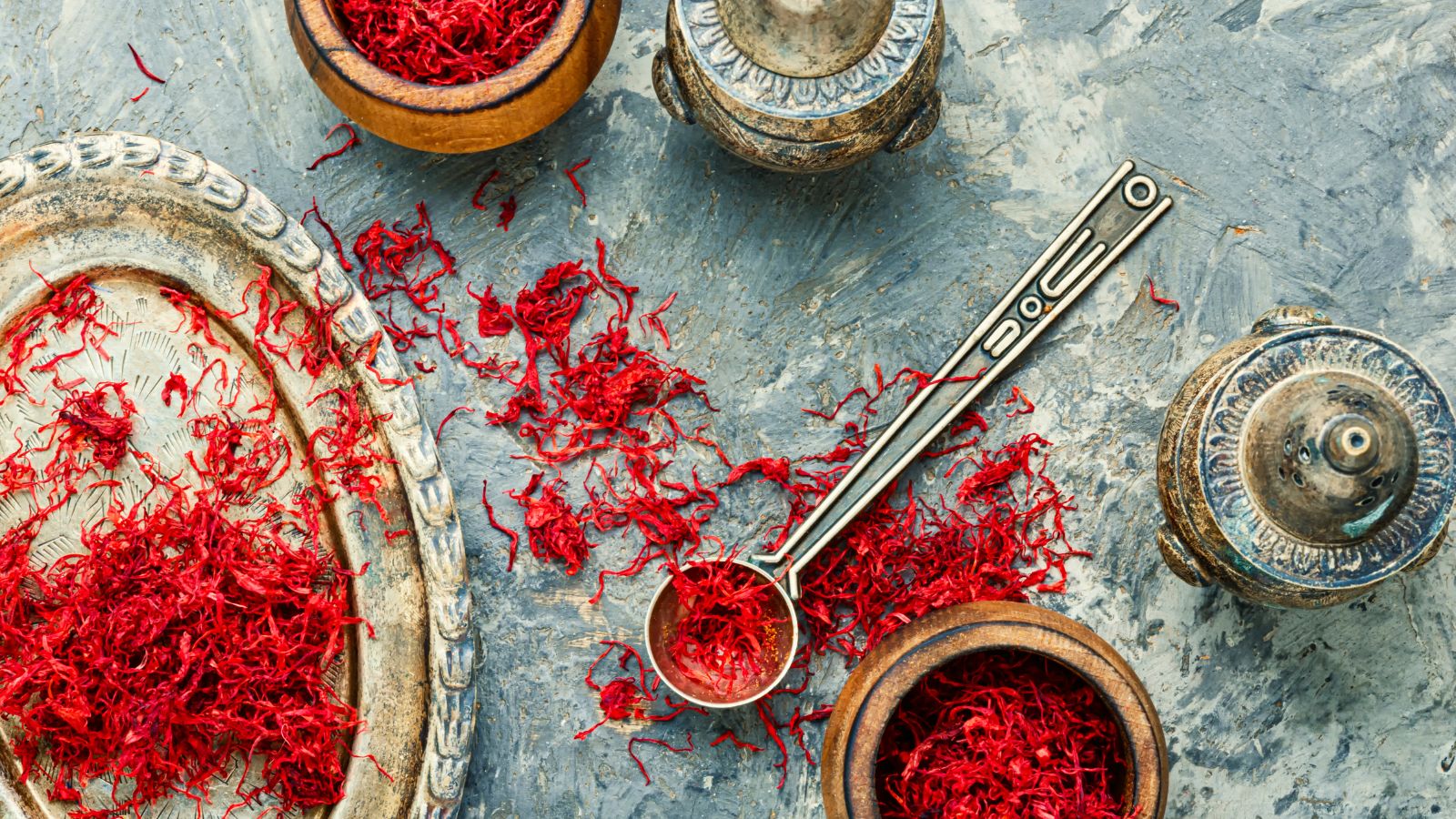Loose saffron threads on a tray with vintage spice tools around.