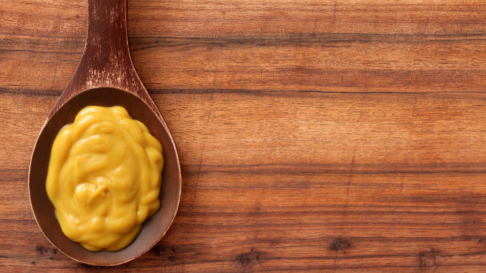 Brown mustard served on wooden spoon on wood background.