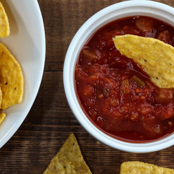Red salsa dip with tortilla chips served in a white bowl.
