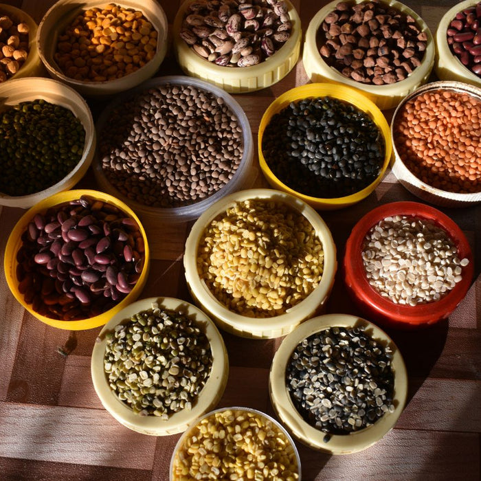 Various dried beans and lentils in colorful bowls on wooden surface.