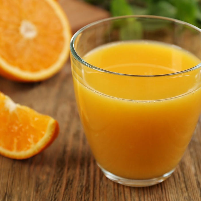 Glass of fresh orange juice with orange slices nearby.