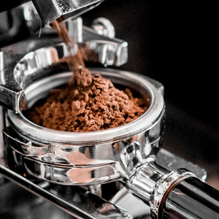 Espresso machine dispensing freshly ground coffee into portafilter.