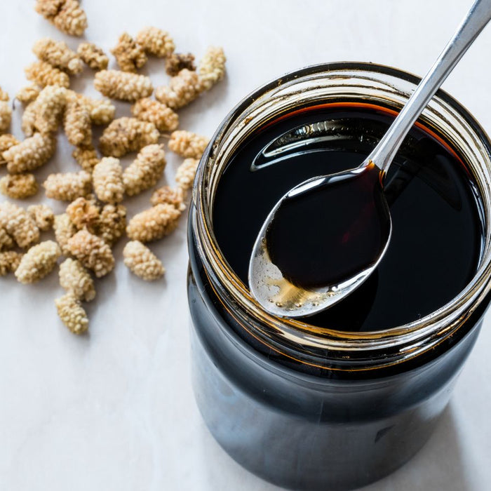 Jar of dark molasses with a spoon and dried ingredients on a white surface.