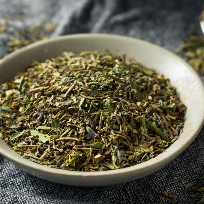 Herbs de Provence in a ceramic bowl on a gray cloth surface.