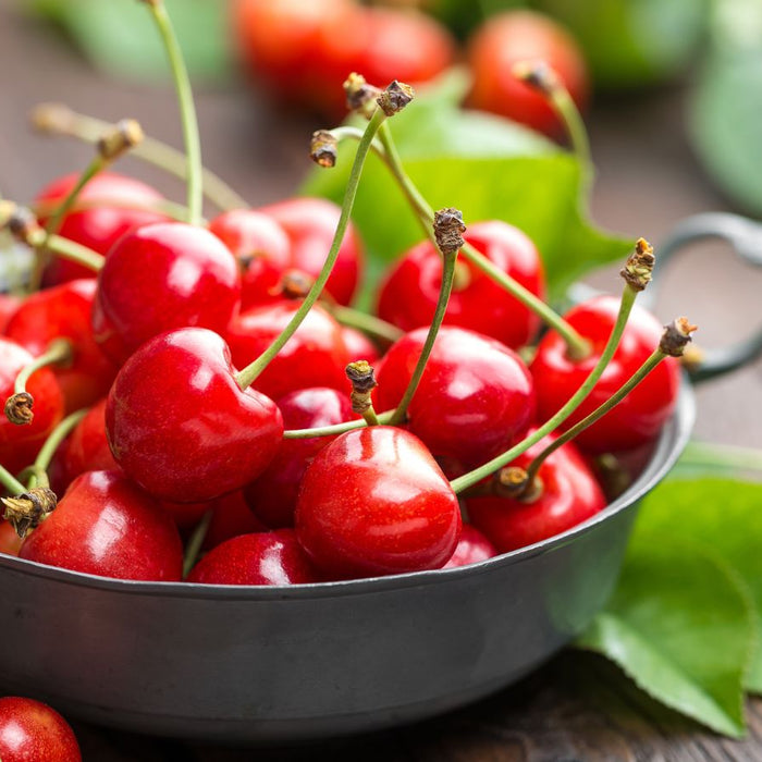 Fresh red cherries in a metal bowl with green leaves on wooden table