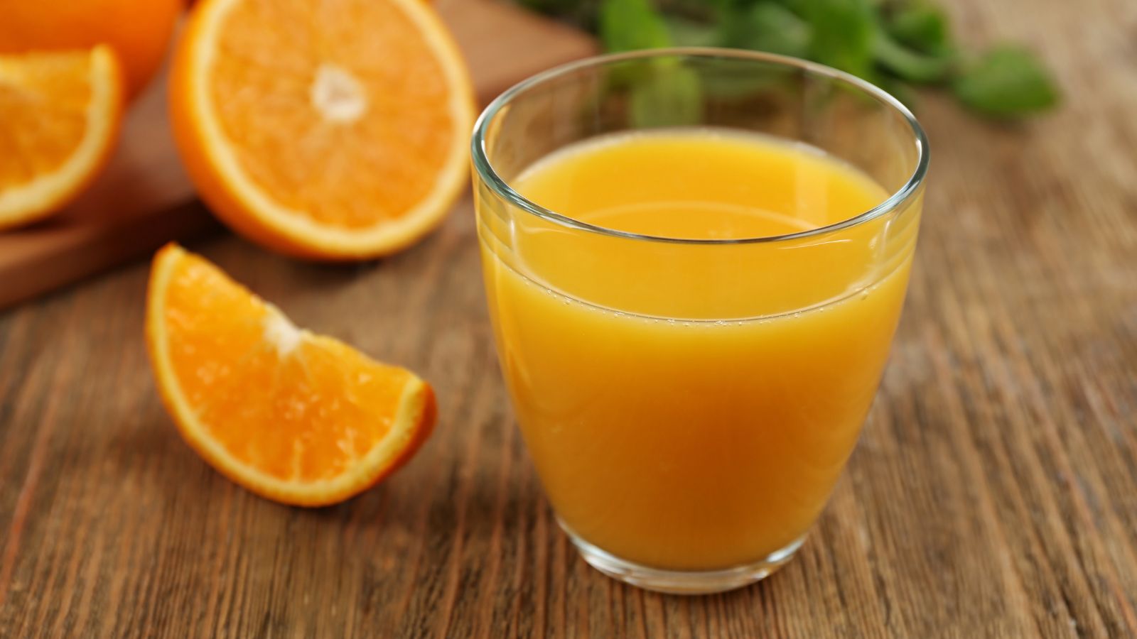 Glass of fresh orange juice with orange slices nearby.
