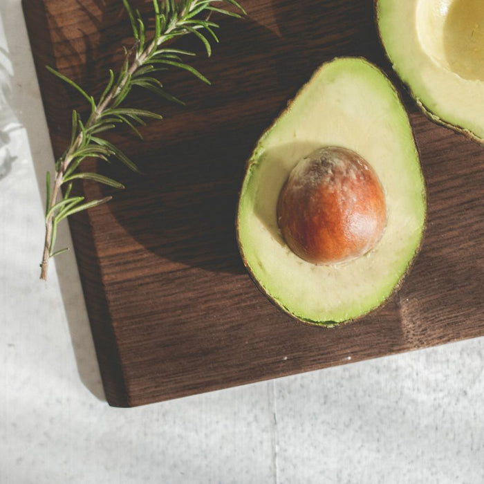 Avocado halves with seed and rosemary sprig on cutting board